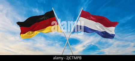 Zwei gekreuzte Flaggen Bundesrepublik Deutschland und Niederlande winken im Wind bei bewölktem Himmel. Konzept von Beziehung, Dialog, Reisen zwischen zwei Cou Stockfoto
