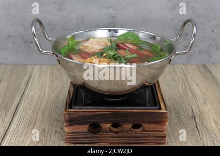 Zauberhafter, glänzender Aufsatz mit Wontonsuppe, der dampfend und verzehrfertig auf dem Topftopf serviert wird. Stockfoto