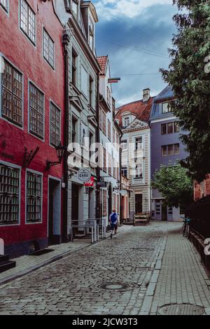 Junger Mann, der an bunten Gebäuden in der Altstadt von Riga vorbeiläuft. Stockfoto