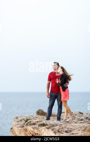 Porträt eines hübschen Paares mittleren Alters, das neben den Copyspace schaut und sich umarmt, während es am Rand der Felsklippe am Meer steht. Stockfoto