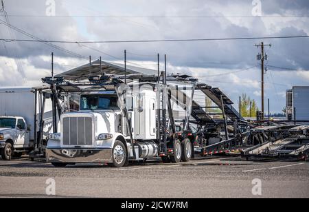 Unbeladener großer LKW-Schlepper mit weißem LKW-Schlepper und leerem modularen hydraulischen Sattelauflieger, der auf dem Industrieparkplatz mit einem anderen LKW steht Stockfoto