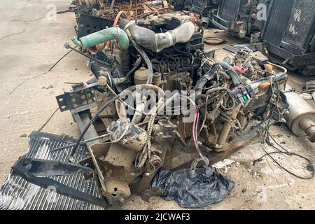 Nahaufnahme eines Verbrennungsmotors, der aus einem Auto entfernt wurde und bei einem Autowrack auf dem Boden ruht Stockfoto