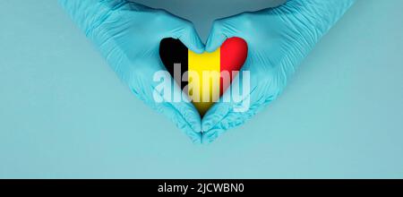 Ärzte Hände tragen blaue OP-Handschuhe, die hören Form Symbol mit Belgien Flagge Stockfoto