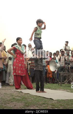 Kinder, die vor Dutzenden von Zuschauern auf einem Feld am Straßenrand am Stadtrand von Rajgir in Bihar, Indien, einen Gymnastikstunt durchführen. Stockfoto