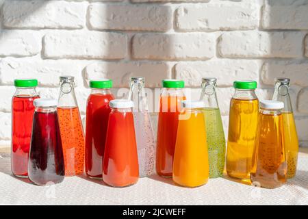 Reihe von Glasflaschen mit verschiedenen Säften gegen weiße Ziegelwände Stockfoto