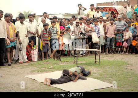 Kinder, die vor Dutzenden von Zuschauern auf einem Feld am Straßenrand am Stadtrand von Rajgir in Bihar, Indien, einen Gymnastikstunt durchführen. Stockfoto