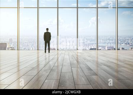 Geschäftserfolg, Führung und Inspiration Konzept mit Geschäftsmann Rückansicht Blick auf die Skyline der Stadt durch großes Fenster in leeren geräumigen Halle mit Stockfoto