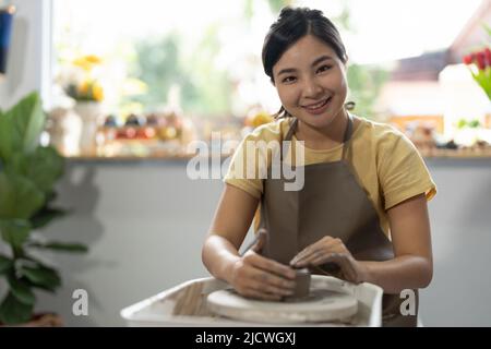 Die Hände einer jungen asiatischen Frau sind aus der Nähe, das meisterhafte Keramikstudio arbeitet mit Ton auf einem Töpferrad. Stockfoto