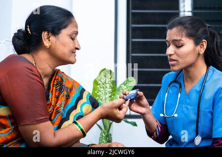 Krankenschwester zu Hause, die Diabetes von kranken Frauen im Alter zwischen 2 und 4 Jahren mit Glucometer untersucht - Konzept der Hausgesundheitsprüfung, Hausmeister und Beruf. Stockfoto