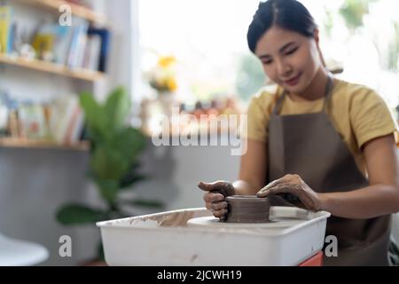 Die Hände einer jungen asiatischen Frau sind aus der Nähe, das meisterhafte Keramikstudio arbeitet mit Ton auf einem Töpferrad. Stockfoto