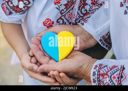 Großmutter hält in ihren Händen ein Herz in der Farbe der ukrainischen Flagge. Selektiver Fokus. Stockfoto