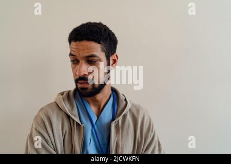 Deprimierter junger männlicher Arzt oder Pflegekraft auf beigem Hintergrund. Stockfoto