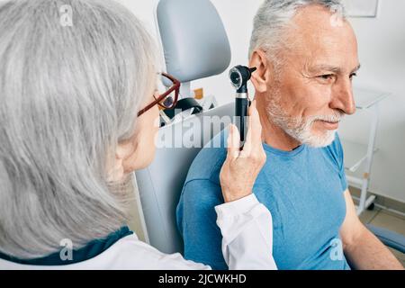Der Arzt des Otolaryngologen überprüft das Ohr des älteren Mannes mit Hilfe des Otoskopes oder des Ohrhörers in der Hörzentrale. Audiologie Stockfoto