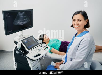 Porträt eines Ultraschallforschers in der Nähe des Ultraschallgeräts in der medizinischen Klinik während der Ultraschalluntersuchung des weiblichen Körpers. Beruf des Ultraschallforschers Stockfoto