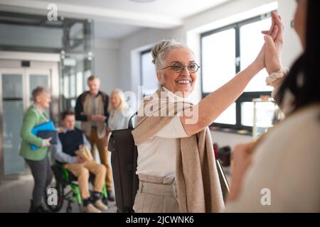 Glückliche ältere Studentinnen treffen sich im Korridor an der Universität mit hohen Fünffälern. Stockfoto