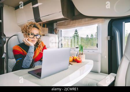 Off Grid Van Life und digitaler Nomadenlebensstil. Nette moderne Frau arbeitet auf Laptop in einem Wohnmobil mit Natur und Freiheit szenischen Ort außerhalb Th Stockfoto