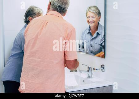 Kaukasisches Paar im älteren Alter im Badezimmer zu Hause, das sich die Hände wascht. Fröhliche, reife Leute, die sich morgens fertig machen. Hotel und Haus leben wirklich für ret Stockfoto