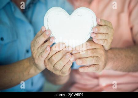 Nahaufnahme des herzförmigen Holzdekorationsoobjekts. Konzept eines gesunden Senior-Lebensstils. Herzinfarktkonzept. Liebe und Beziehung mit alten reifen Mann Stockfoto
