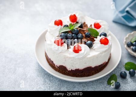 Schokoladenkuchen, weißer Käsekuchen mit Heidelbeeren, Kirsche, brauner Schokolade und Schlagsahne Stockfoto
