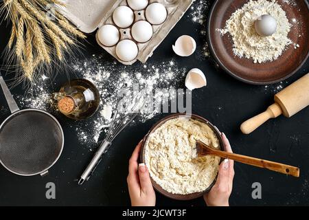 Weibliche Hände machen/Mixing Teig in brauner Schale auf Schwarzen Tisch, backen Vorbereitung close-up. Stockfoto