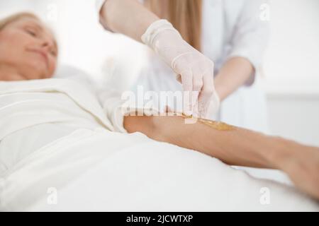 Frau mit Haarentfernung Verfahren am Arm mit Zuckerpaste im Schönheitssalon, Nahaufnahme Stockfoto