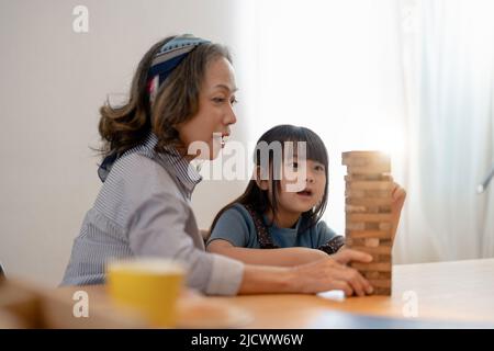 Glückliche Momente der asiatischen Großmutter mit ihrer Enkelin, die Jenga-Konstrukteurin spielt. Freizeitaktivitäten für Kinder zu Hause Stockfoto