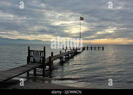Holzpier am Genfer See bei Sonnenuntergang mit Schweizer Flagge und Silhouette der Berge am Horizont Stockfoto