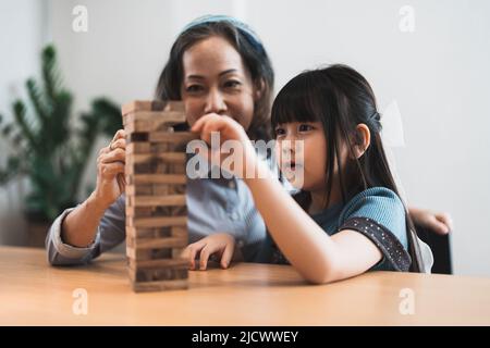 Glückliche Momente der asiatischen Großmutter mit ihrer Enkelin, die Jenga-Konstrukteurin spielt. Freizeitaktivitäten für Kinder zu Hause. Stockfoto