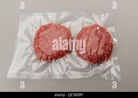 Burger-Fleisch für Hamburger in vakuumverpackter, versiegelter Verpackung für Sous-Vide-Garen isoliert auf grauem Hintergrund Stockfoto