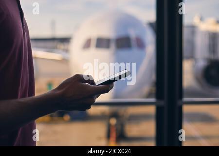 Silhouette der Hand des Passagiers während der Nutzung des Mobiltelefons während der Wartezeit im Flughafenterminal. Stockfoto