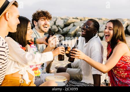 Glückliche Freunde genießen das Wochenende am Strand und jubeln mit Bieren Stockfoto