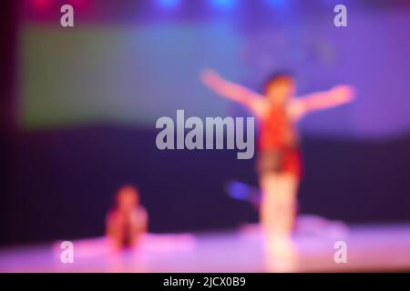 Silhouetten von kleinen Tänzern mit Elementen des gymnastischen Tanzes. Farbiger unscharfer Hintergrund des Tanzfestivals. Helle Bühnenbeleuchtung. Hochwertige Fotos Stockfoto