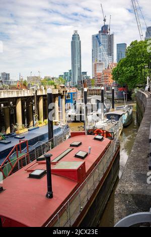 Wohnboote vertäuten in Nine Elms, Vauxhall, London mit dem Tower in der Ferne. Stockfoto