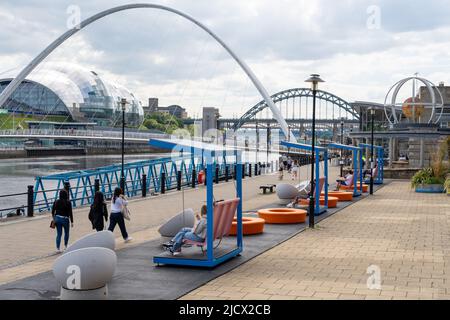 Blick auf den Quayside, Newcastle Upon Tyne, Großbritannien, mit Tyne-Brücken, einschließlich Gateshead Millennium Bridge und hellen modernen Sitzgelegenheiten. Stockfoto