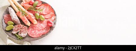 Banner mit italienischem Antipasti-Menü. Wurstplatte mit verschiedenen Wurstsorten - Salami, bresaola, Proscuitto, serviert mit Oliven und Grissini Stockfoto