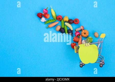 Metall-Einkaufswagen mit Obst und Gemüse auf blauem Hintergrund. Mini-Einkaufswagen für Spielzeug Stockfoto