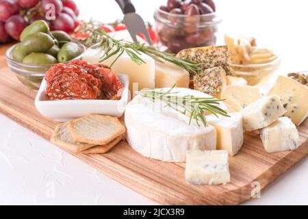 Käseplatte mit verschiedenen Käsesorten, serviert mit Oliven, sonnengetrockneten Tomaten und Kräutern auf weißem Tischhintergrund. Käseplatte für Aperitif Stockfoto