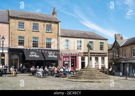 Menschen, die vor einem Café auf dem Alnwick Market Square, Northumberland, England, Großbritannien, sitzen Stockfoto