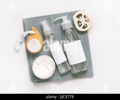 Hausgemachte Kosmetik in Plastikgläsern und Flaschen auf grauem Handtuch oben auf weißem Tisch. Modell der Markenverpackung. Bio-Naturkosmetik für Haut und ha Stockfoto