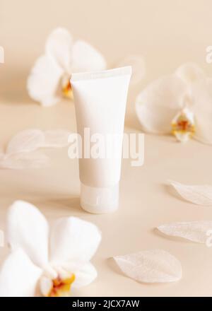 Weiße Plastik-cremefarbene Röhre in der Nähe von weißen Orchideenblüten auf hellgelb, Nahaufnahme, Mockup. Hautpflegeprodukt, Creme oder Lotion. Exotische Naturkosmetik Stockfoto