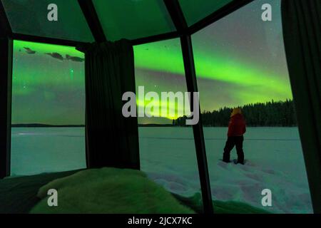 Person, die im Schnee steht und Aurora Borealis (Nordlichter) anschaut, Blick durch Glasfenster von Iglu, Jokkmokk, Lappland, Schweden, Skandinavien Stockfoto