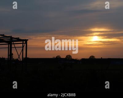 Ein satter, lebendiger Sonnenuntergang, der durch das silhouettierte Skelett eines ausgenutzten Flugzeughangs gesehen wird, wobei ein Vogel im Flug vor den glühenden Wolken hinterleuchtet ist. Stockfoto