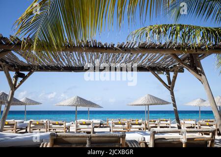 Sonnenliegen aus Holz mit Sonnenschirmen an einem tropischen Strand. Beach Club. Stockfoto