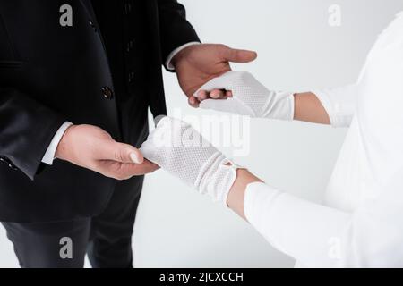 Beschnittene Ansicht von Mann und Frau in Handschuhen, die die Hände isoliert auf Grau halten Stockfoto