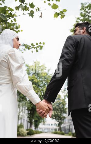 Niedrige Ansicht des Bräutigams und der muslimischen Braut, die die Hände halten Stockfoto