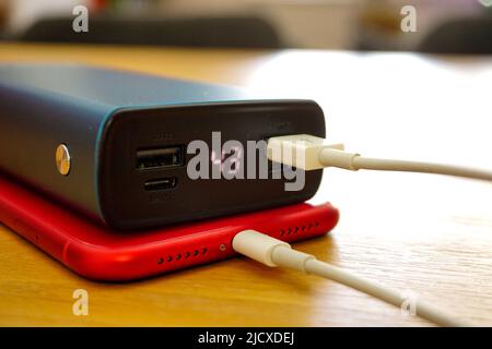 30 April 2021 Eskisehir Türkei. Rotes iphone 11 wird von Powerbank auf Holztisch geladen Stockfoto