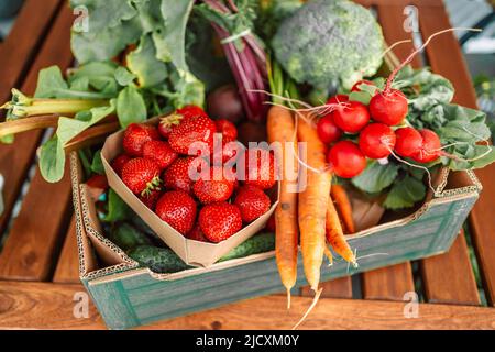 Grüne Holzkiste voller ökologischem, frischem, gesundem Gemüse. Brokkoli Karotten Radieschen Tomate auf Holz Küchentisch. Stockfoto