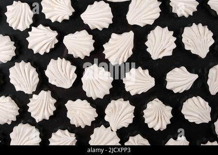 Weiße Baisons auf schwarzem Hintergrund, süßes Gebäck, ein Dessert aus Zucker und Eiweiß. Stockfoto