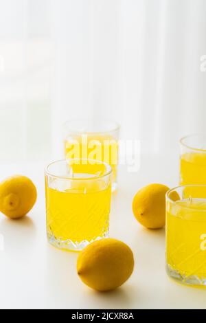 Gläser mit natürlicher Limonade in der Nähe von ganzen Zitronen auf weißem und unscharfem Hintergrund Stockfoto