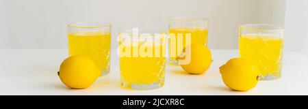Gläser mit frischem Citrus Tonic in der Nähe von ganzen Zitronen auf weißer Oberfläche und grauem Hintergrund, Banner Stockfoto